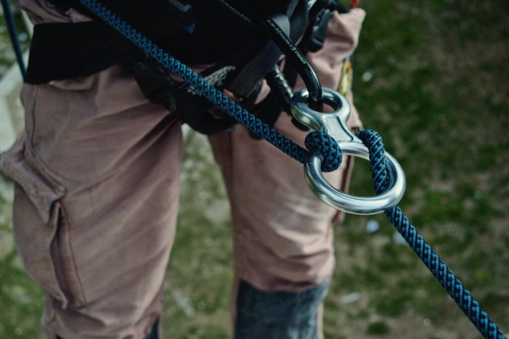 Im Bild ist die untere Hälfte eines Körpers zu sehen, der ein Seil mit Kletterausrüstung an seiner Outdoorhose befestigt hat.